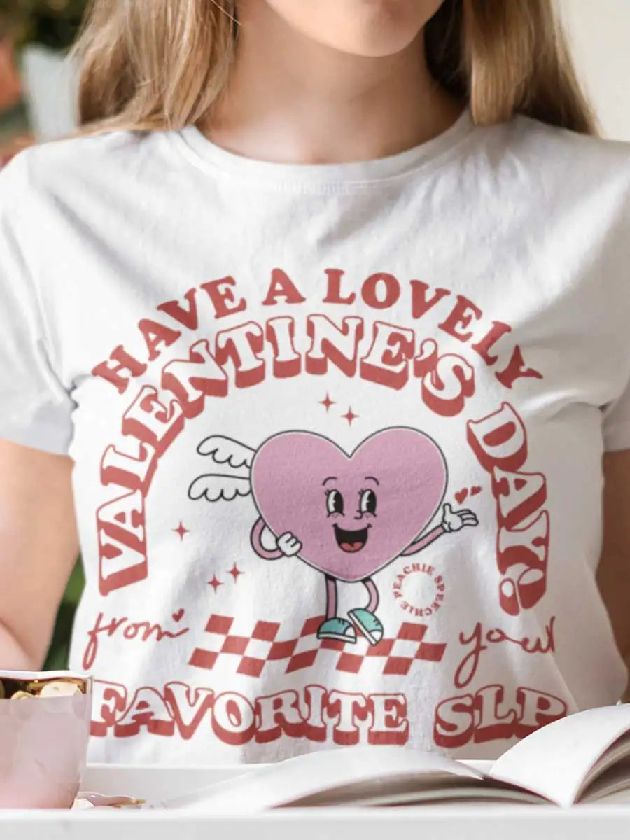 White cotton t-shirt featuring a pink cartoon heart with wings and the text ’have a lovely valentine’s day’ in red, designed by peachy slp.