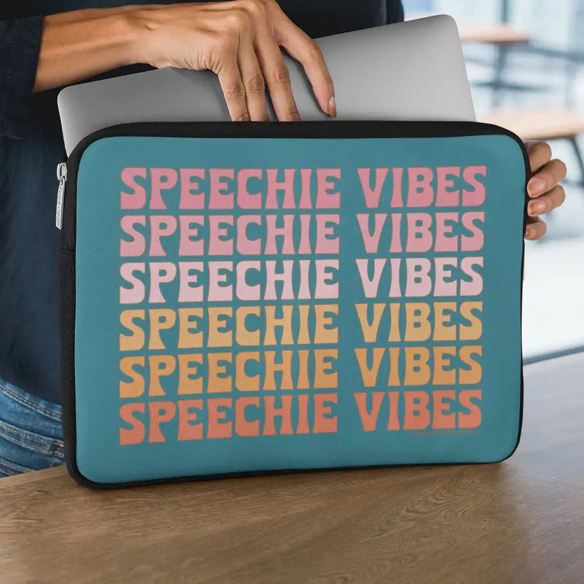 Teal laptop sleeve with repeating ’SPEECHIE VIBES’ text in pink, yellow and coral colors.