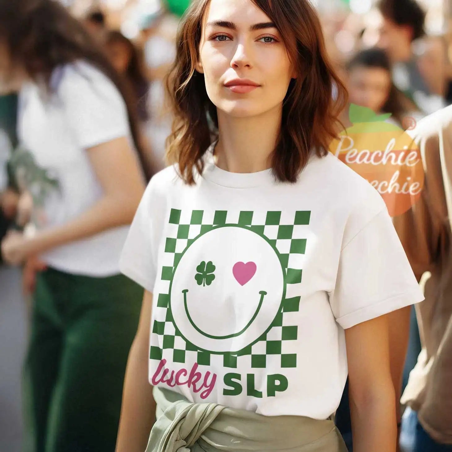 White cotton t-shirt featuring a green and white checkered smiley face design with a shamrock and pink heart, labeled ’lucky slp’ in pink script.